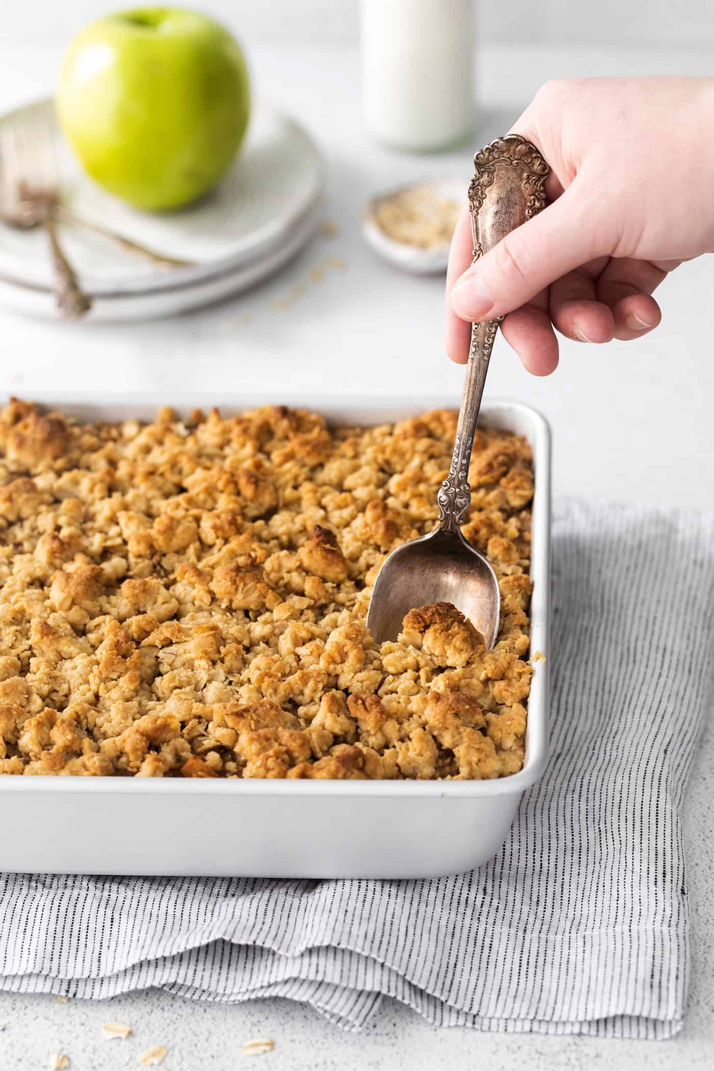 a spoon in a white square baking dish of baked apple oatmeal