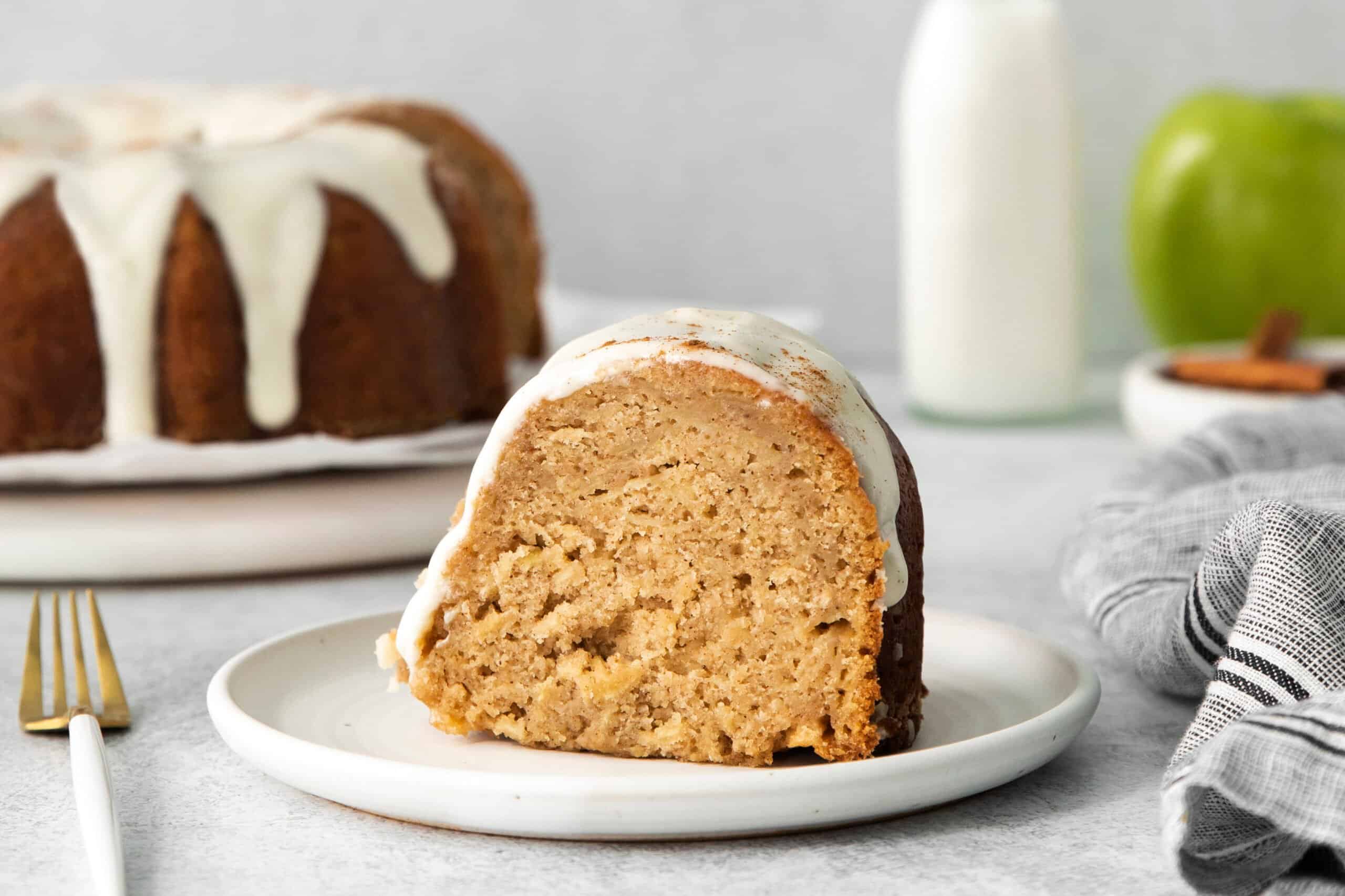 a piece of glazed apple Bundt cake on a small plate, with the whole cake in the background