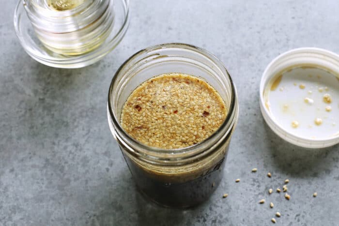 a jar of dressing with sesame seeds floating on top