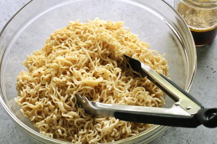 a clear bowl of cooked ramen noodles, with a tongs