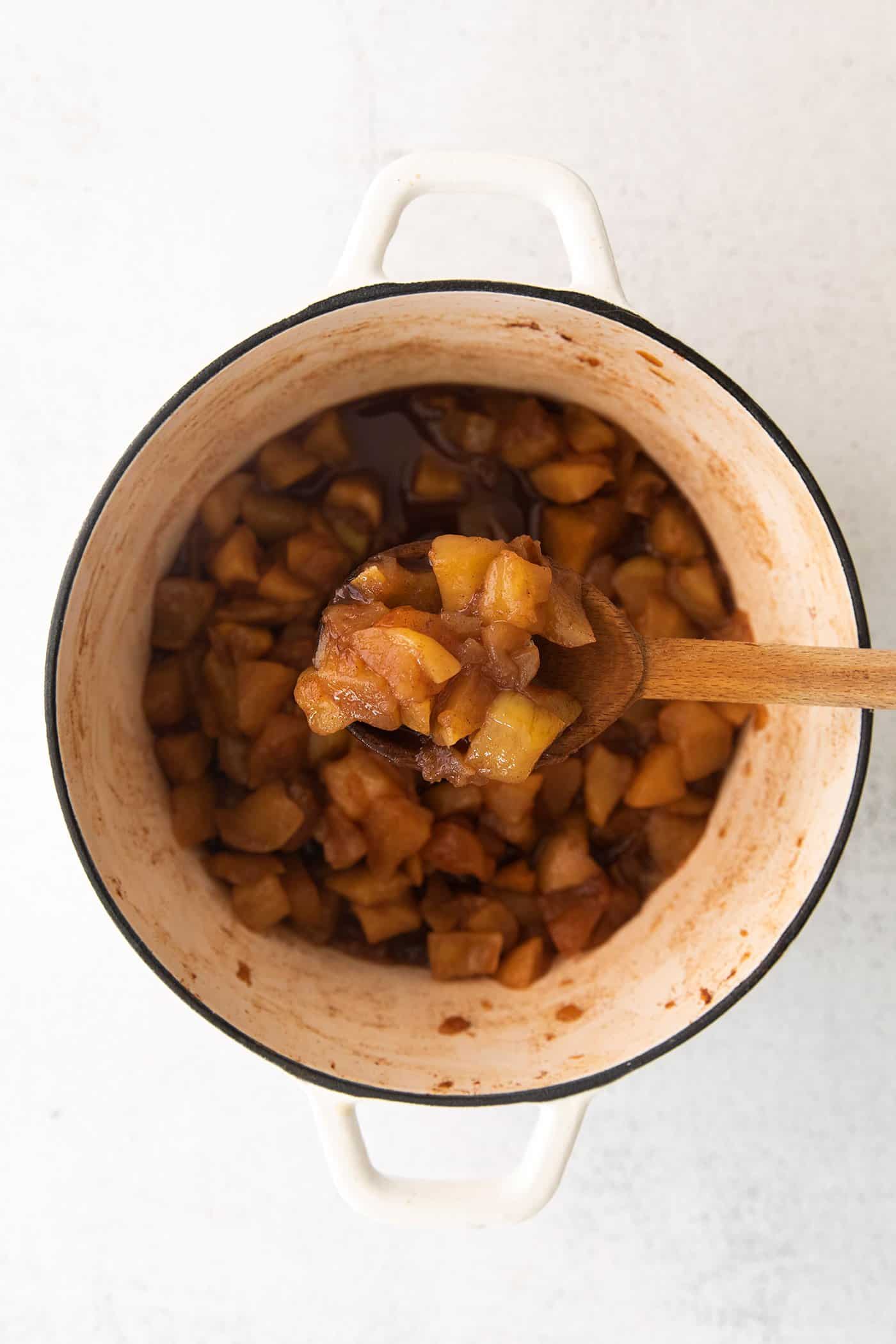 a wooden spoonful of homemade applesauce out of a large white pot