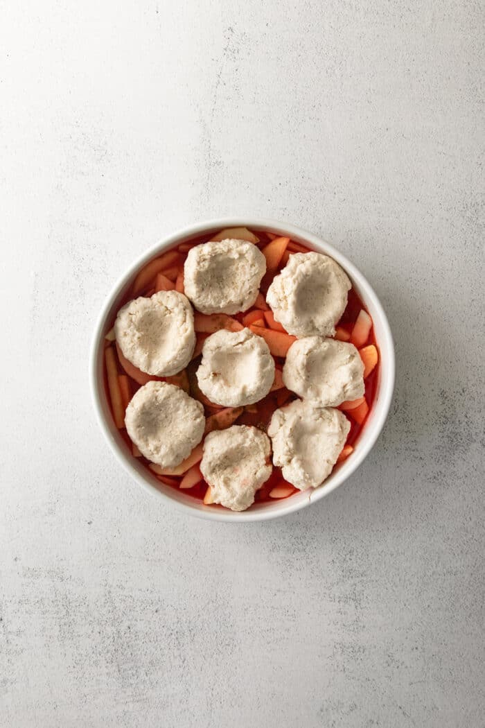 puffs of biscuit dough on top of sliced apples in a round white baking dish