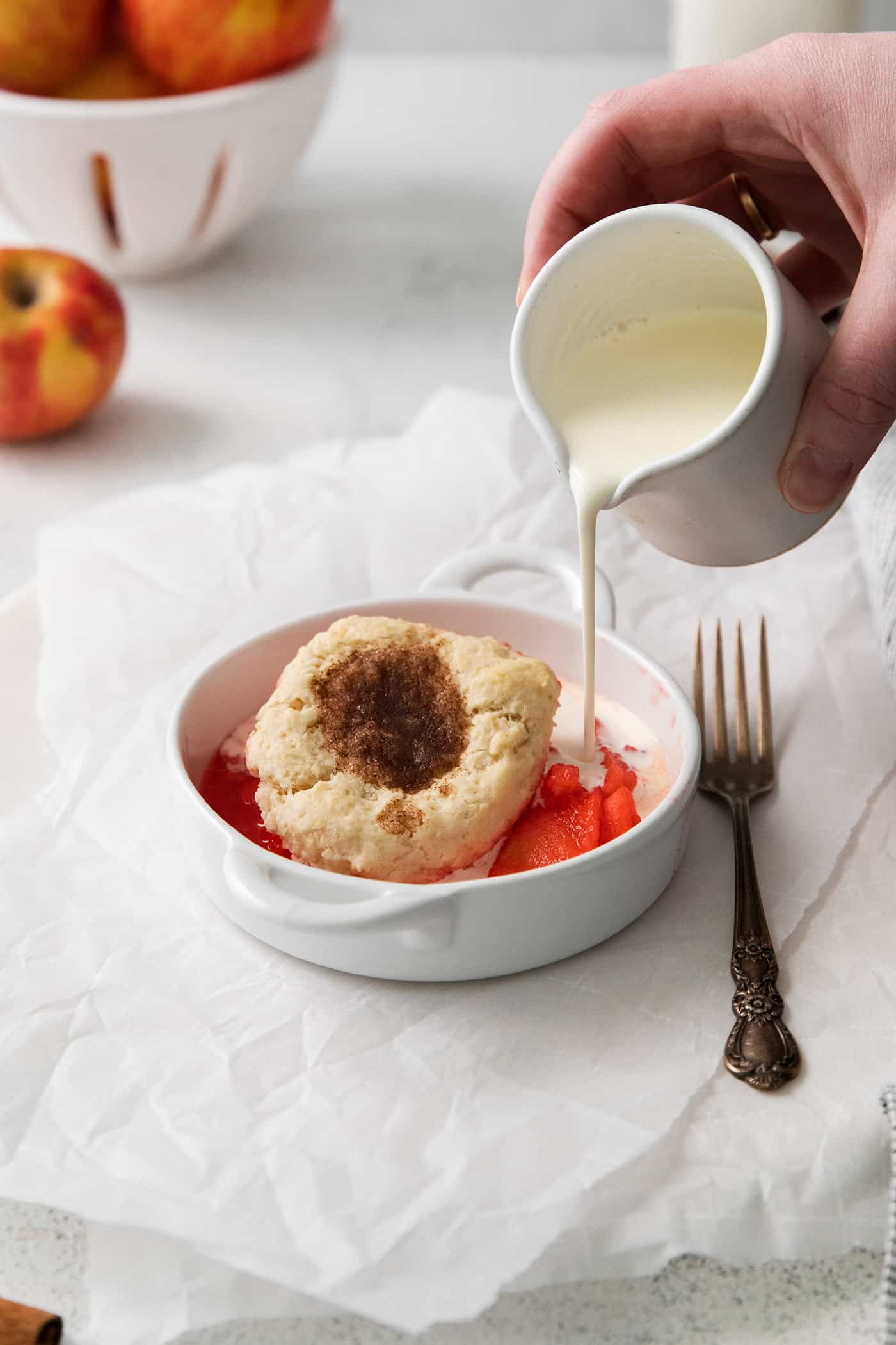 pouring cream into a small bowl of apple dessert