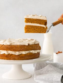 removing a slice of cake from the layered pumpkin cake on a cake stand