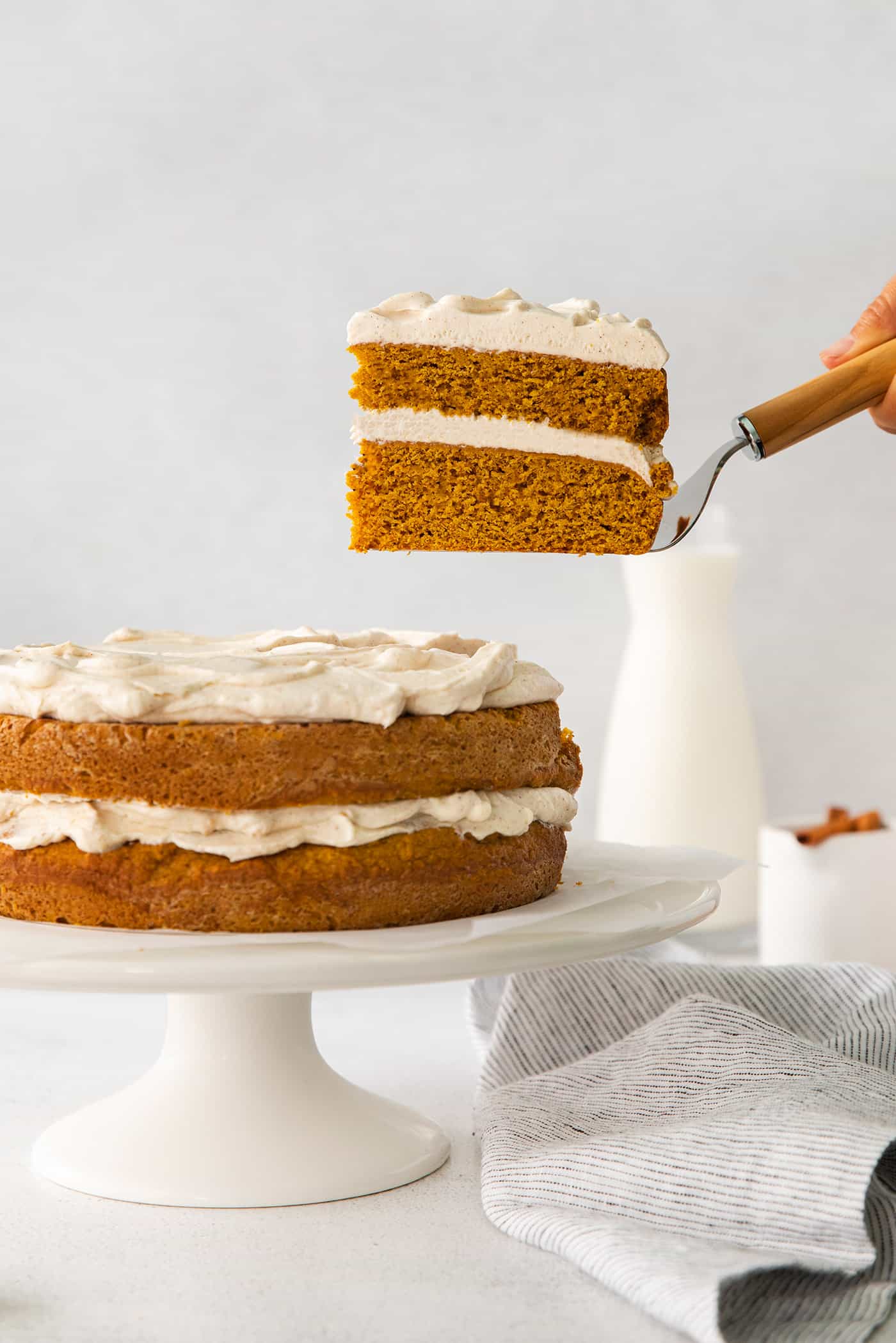 removing a slice of cake from the layered pumpkin cake on a cake stand