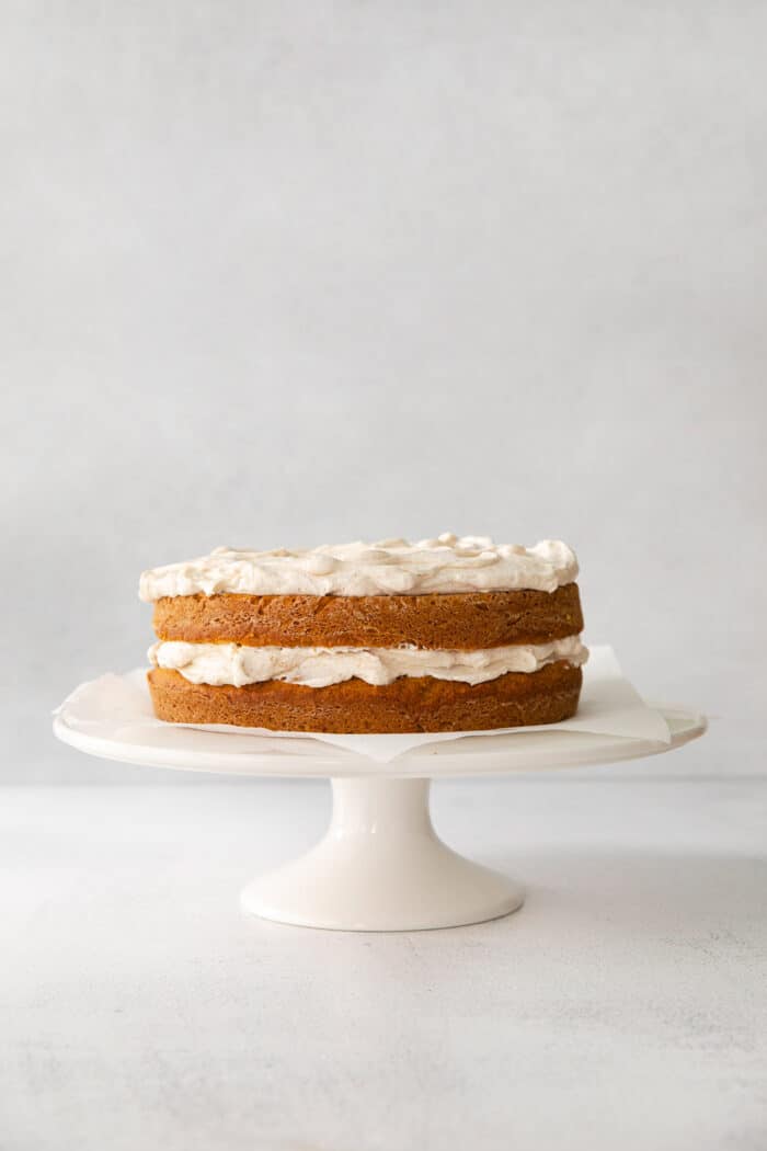 assembled double layer pumpkin cake with a middle and top layer of creamy cinnamon whipped topping, on a cake stand