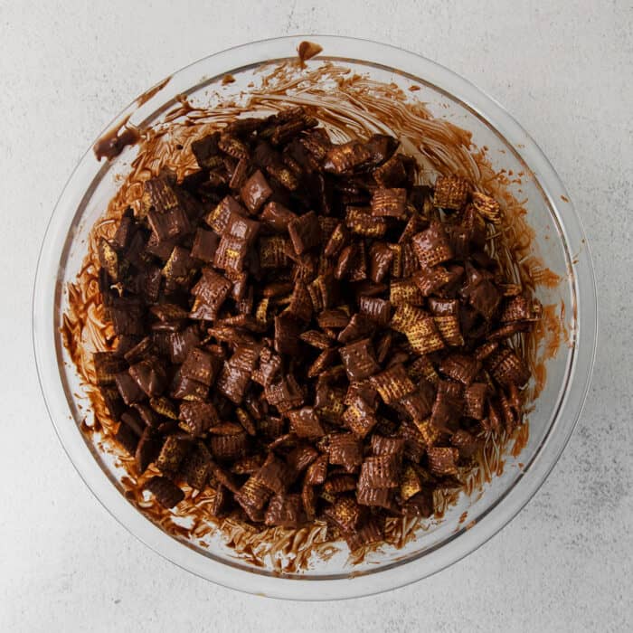 a large clear bowl of Chex cereal covered in a melted chocolate and peanut butter mixture