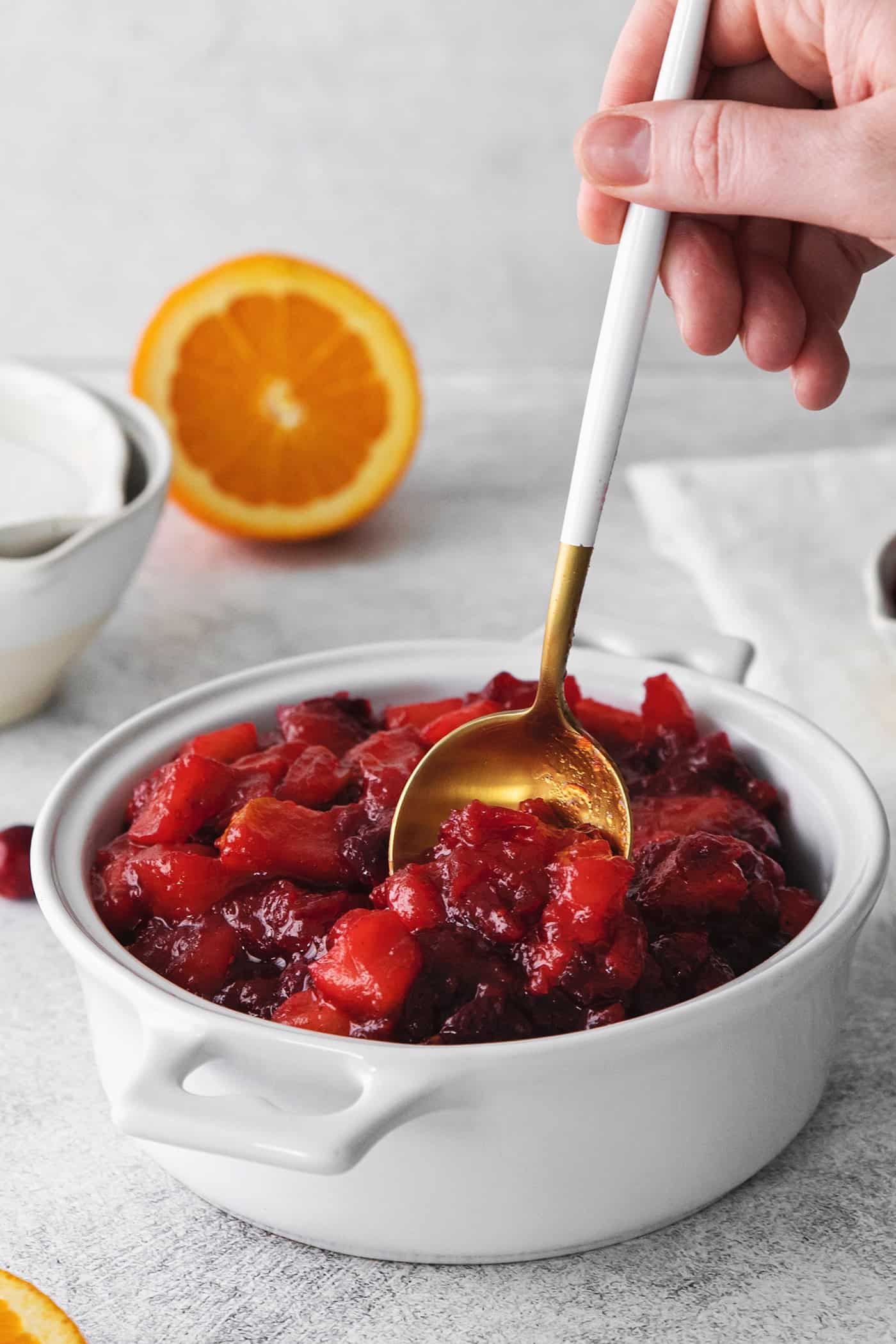 homemade cranberry sauce in a white bowl, with a large gold and white spoon