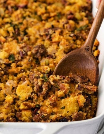 cornbread dressing in a white baking dish, with a wooden spoon digging into it