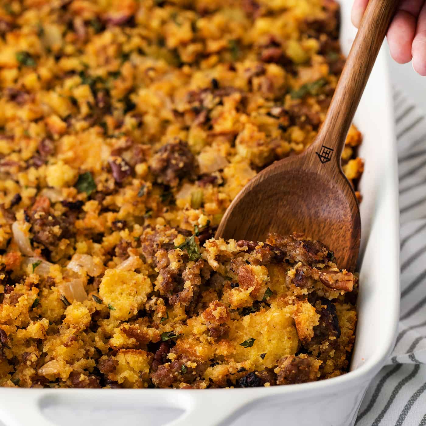 cornbread dressing in a white baking dish, with a wooden spoon digging into it