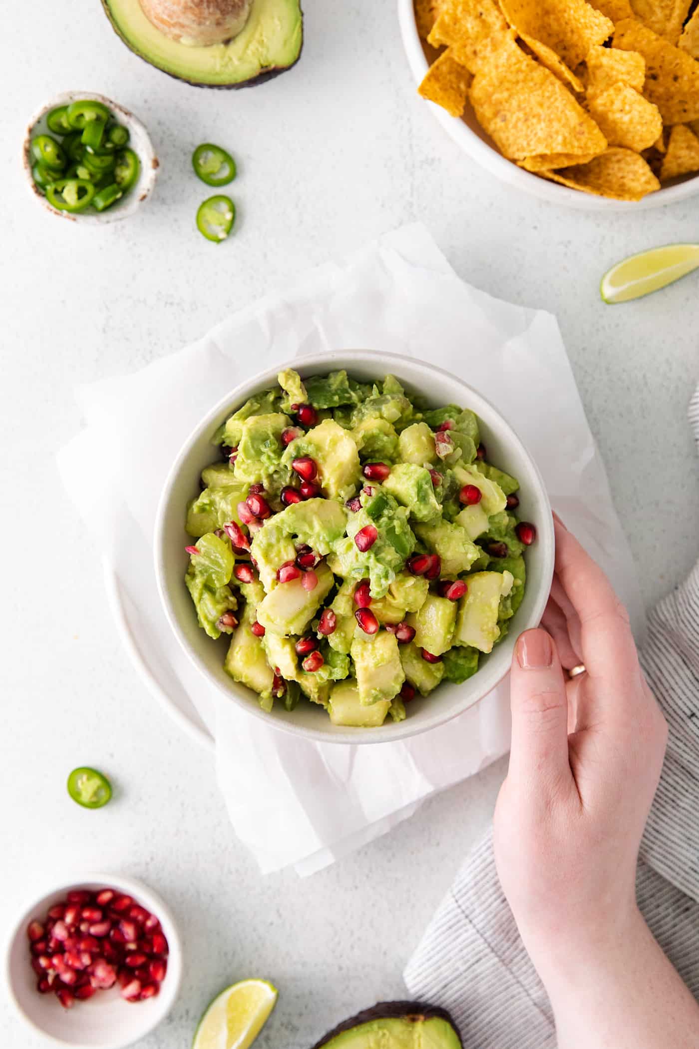 A hand touching a white bowl of holiday guacamole