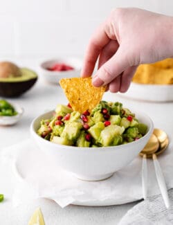 A hand dipping a chip in holiday guacamole