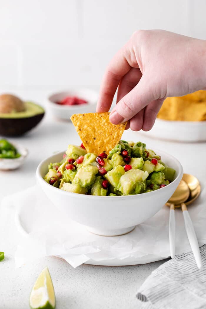 A hand dipping a chip in holiday guacamole