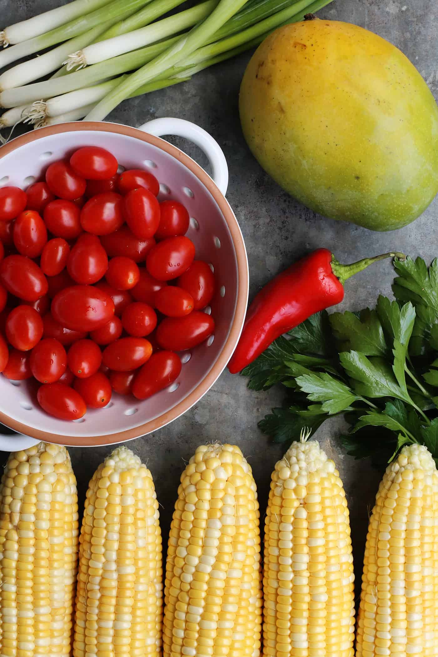 fresh ingredients for salad: sweet corn, mango, tomatoes, chili, green onion, parsley