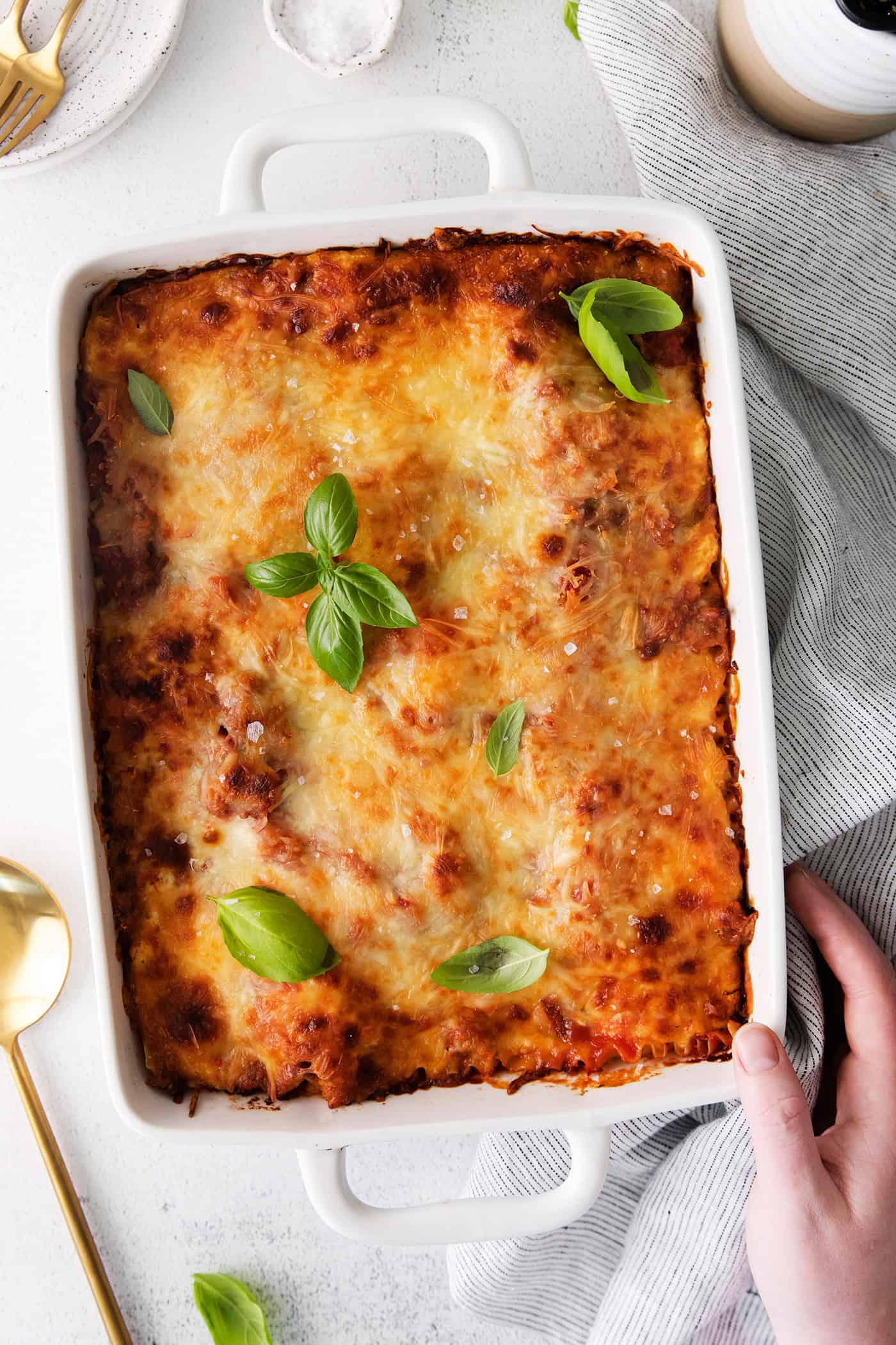 A hand touching a baking dish of lasagna