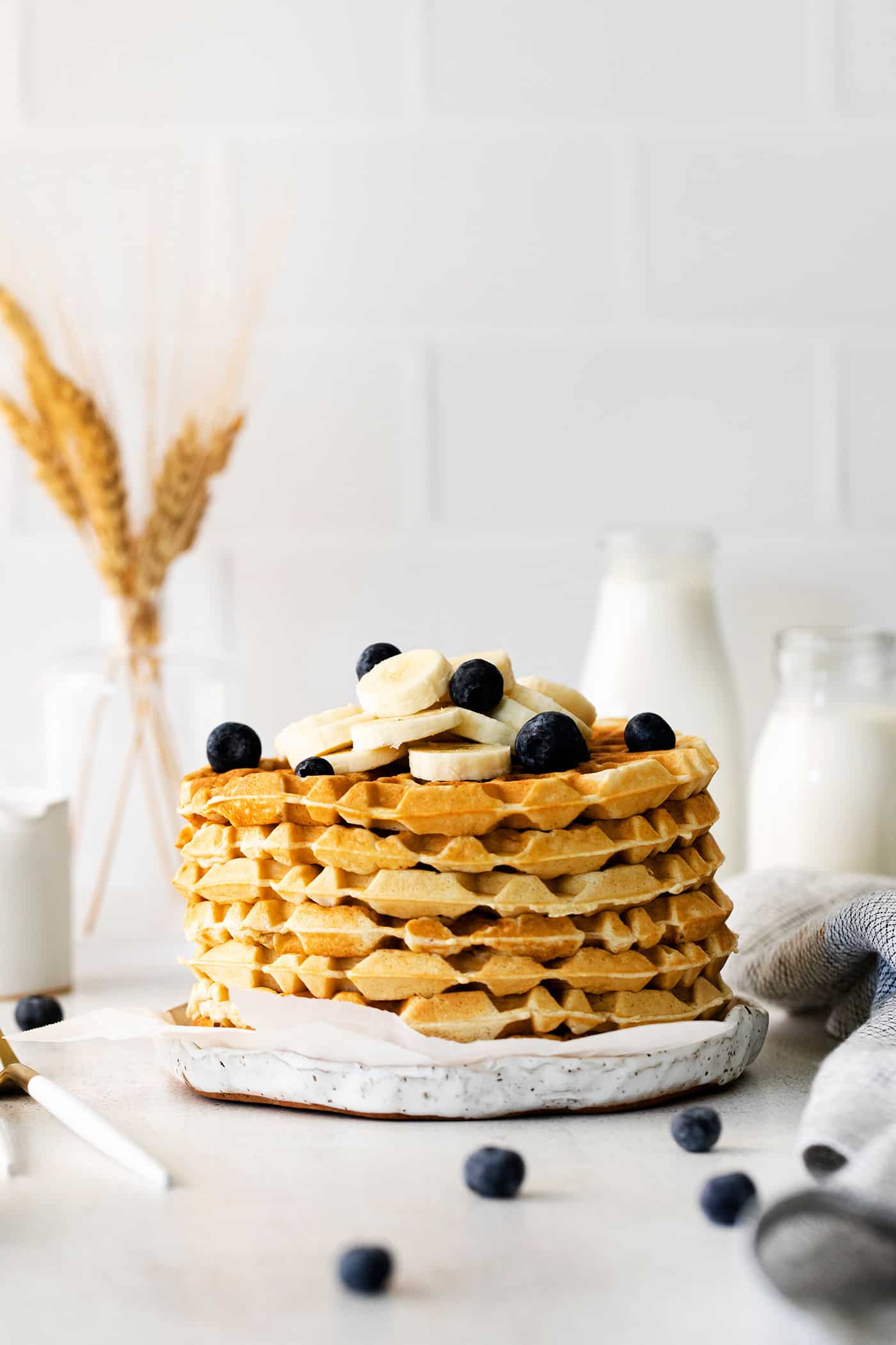 A stack of classic waffles with blueberries and bananas on a white plate