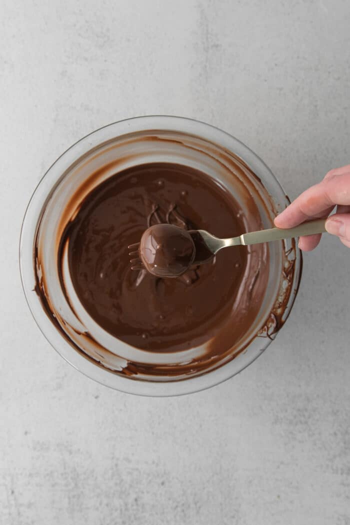 A fork dipping cookie dough truffles in chocolate