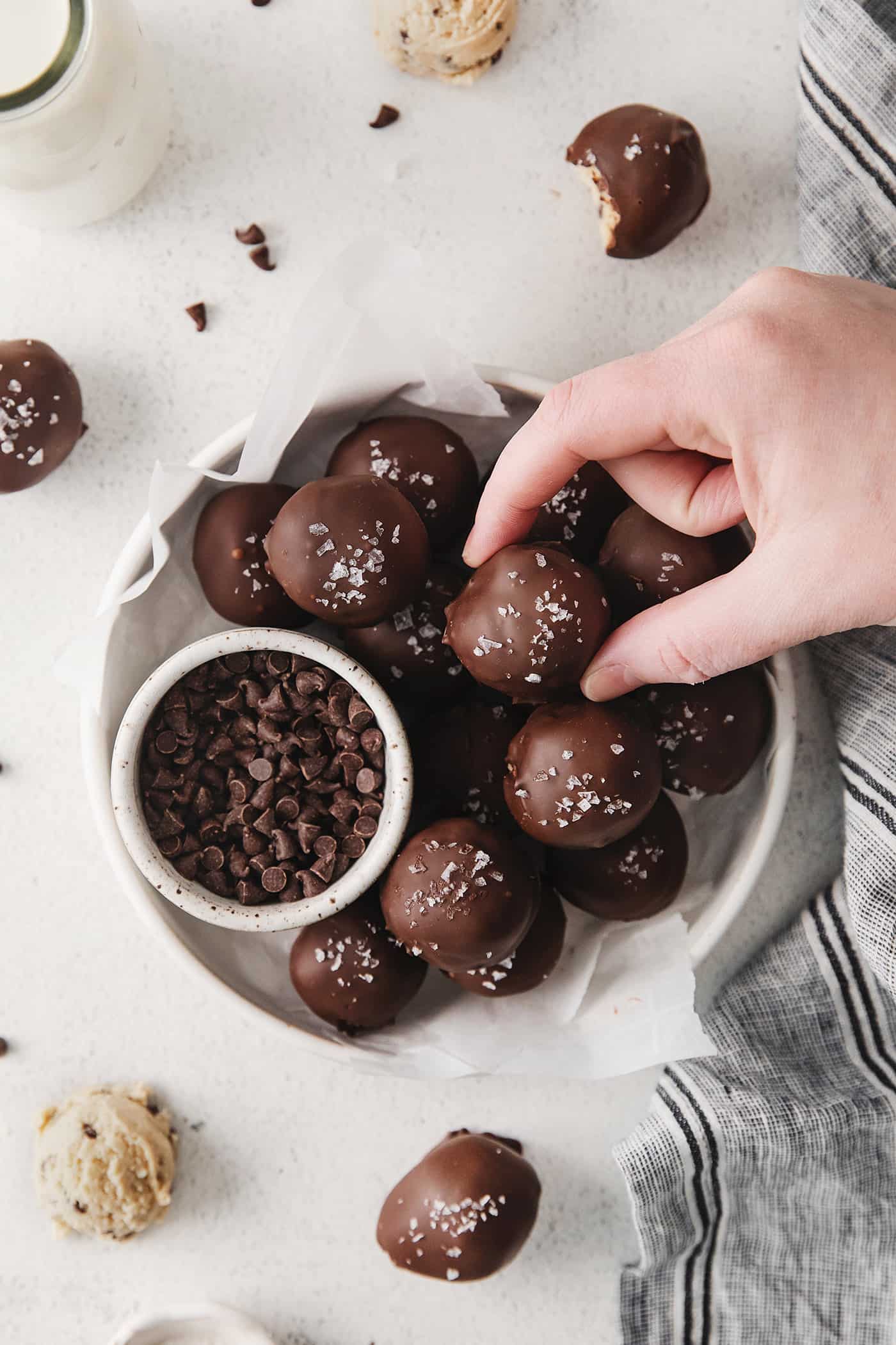 A hand reaching for an edible cookie dough truffle on a plate