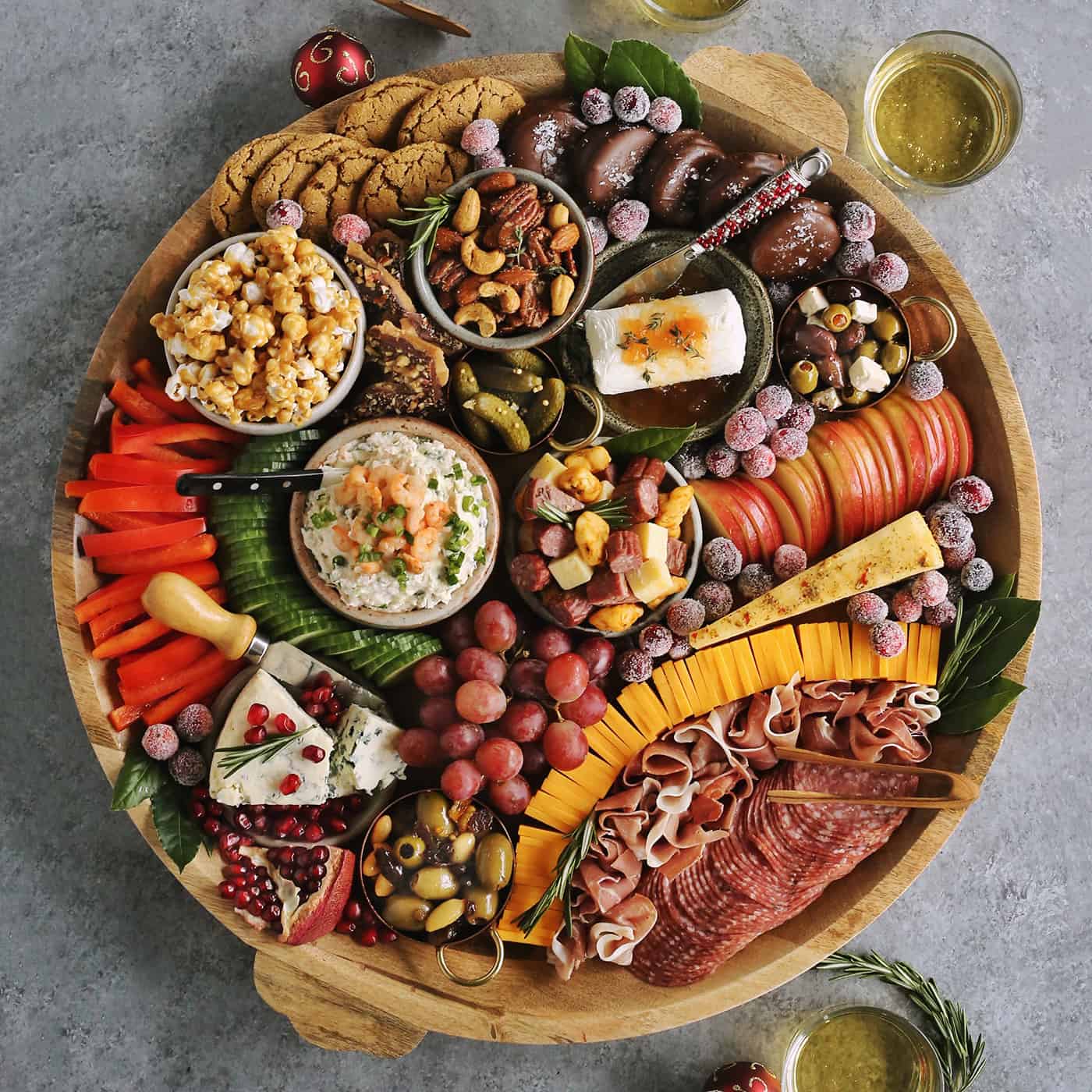 a large round wood charcuterie board full of cheese, meat, olives, sweets, and nuts