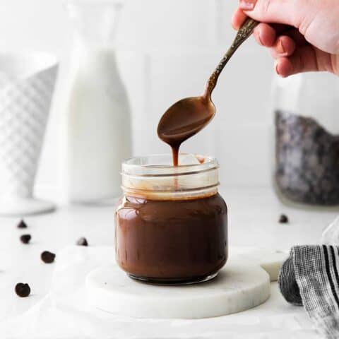 A spoon over a glass jar over hot fudge sauce