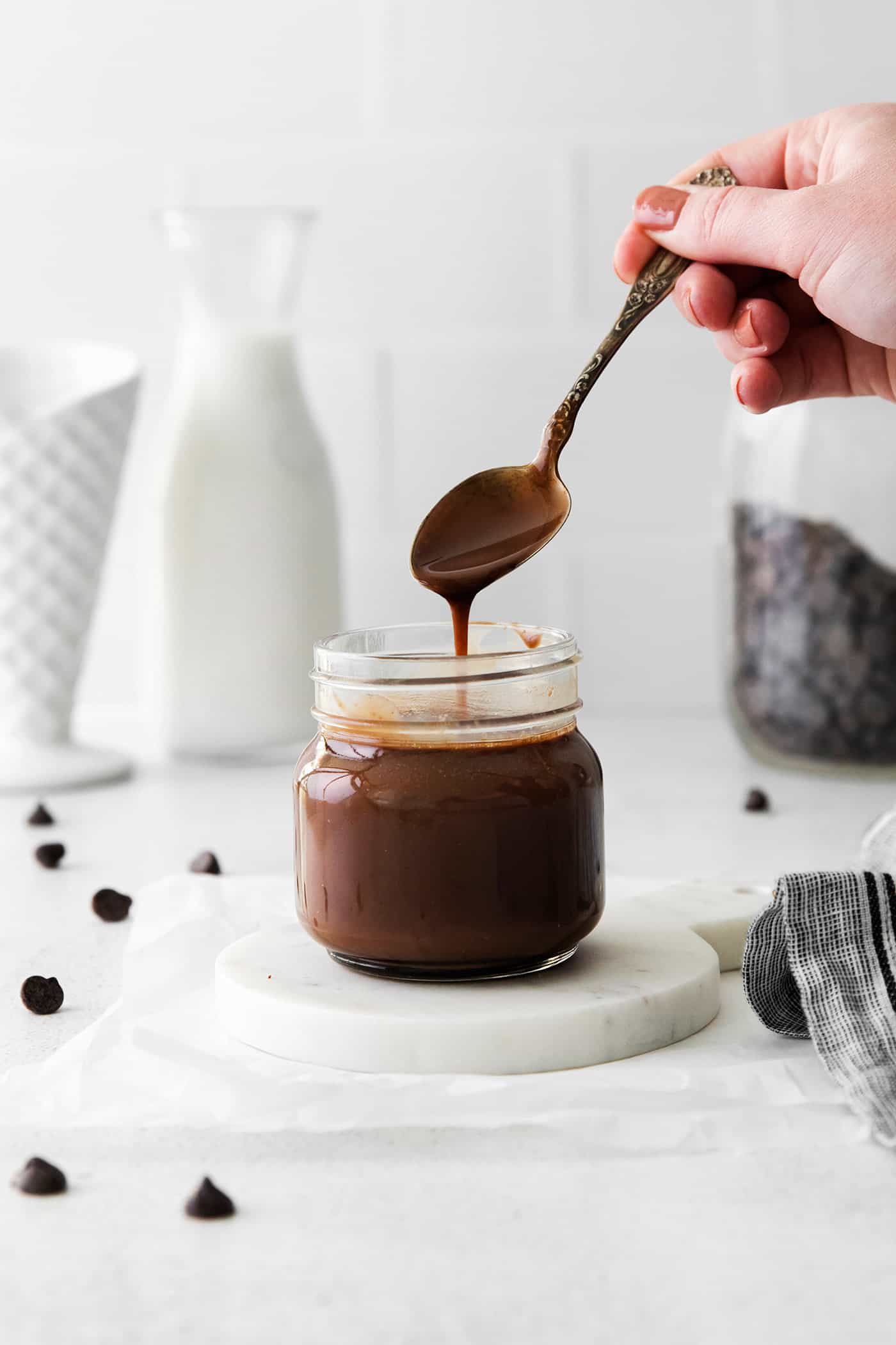 A spoon over a glass jar over hot fudge sauce