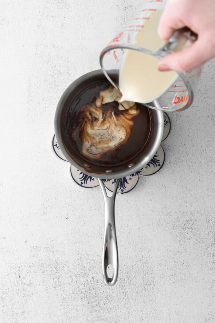 Evaporated milk being poured into a sauce pan with melted chocolate