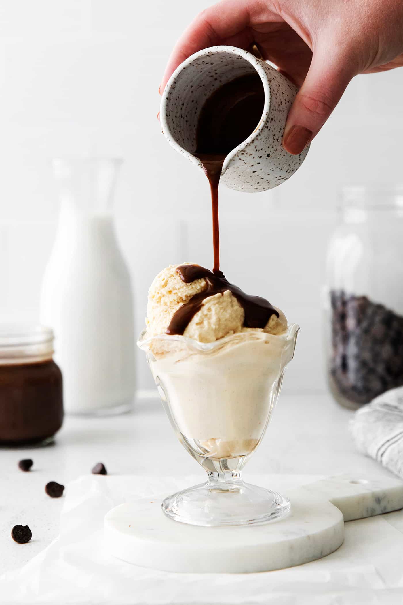A hand pouring hot fudge sauce over scoops of ice cream