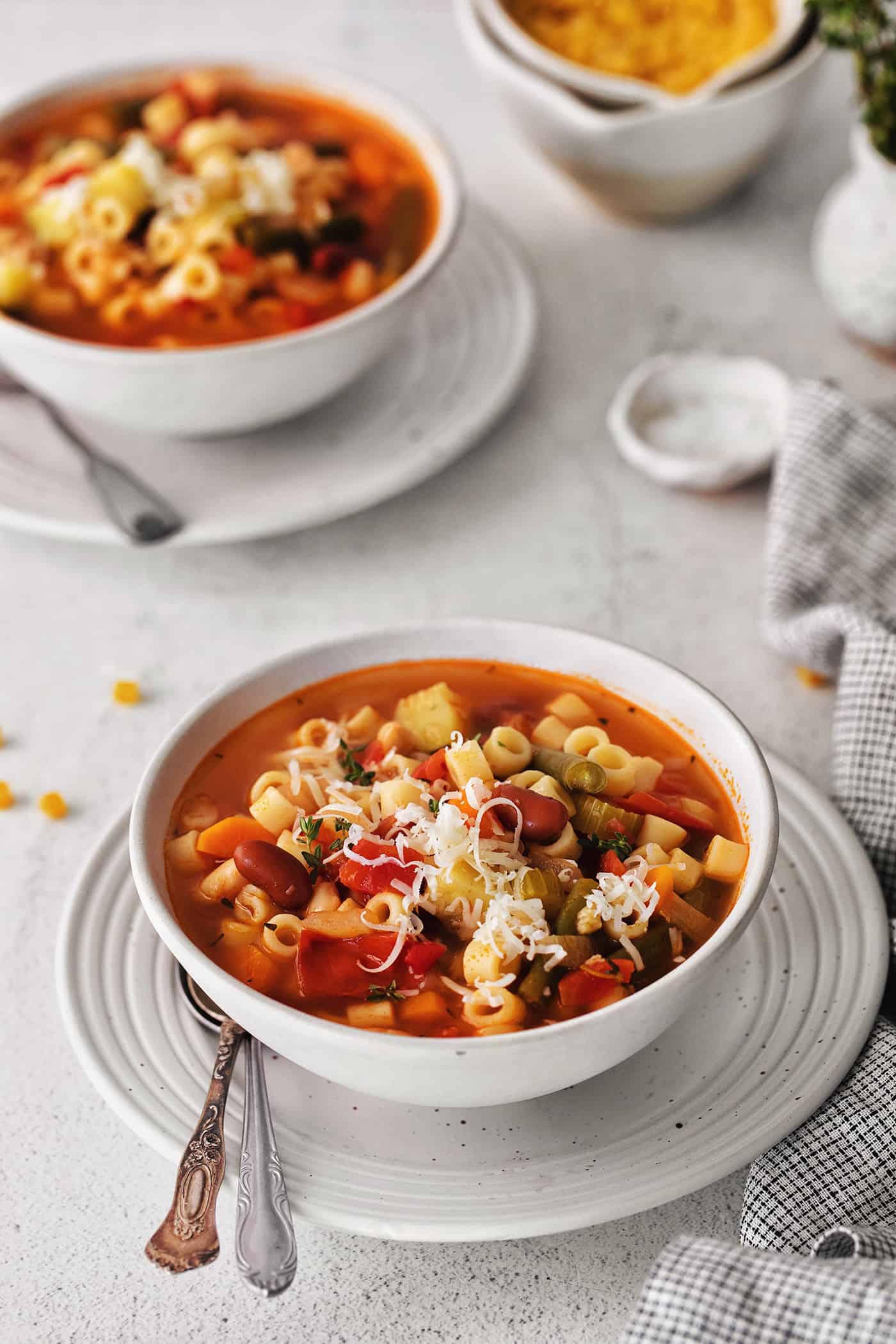 Angled view of a white bowl of minestrone soup with a second bowl in the background