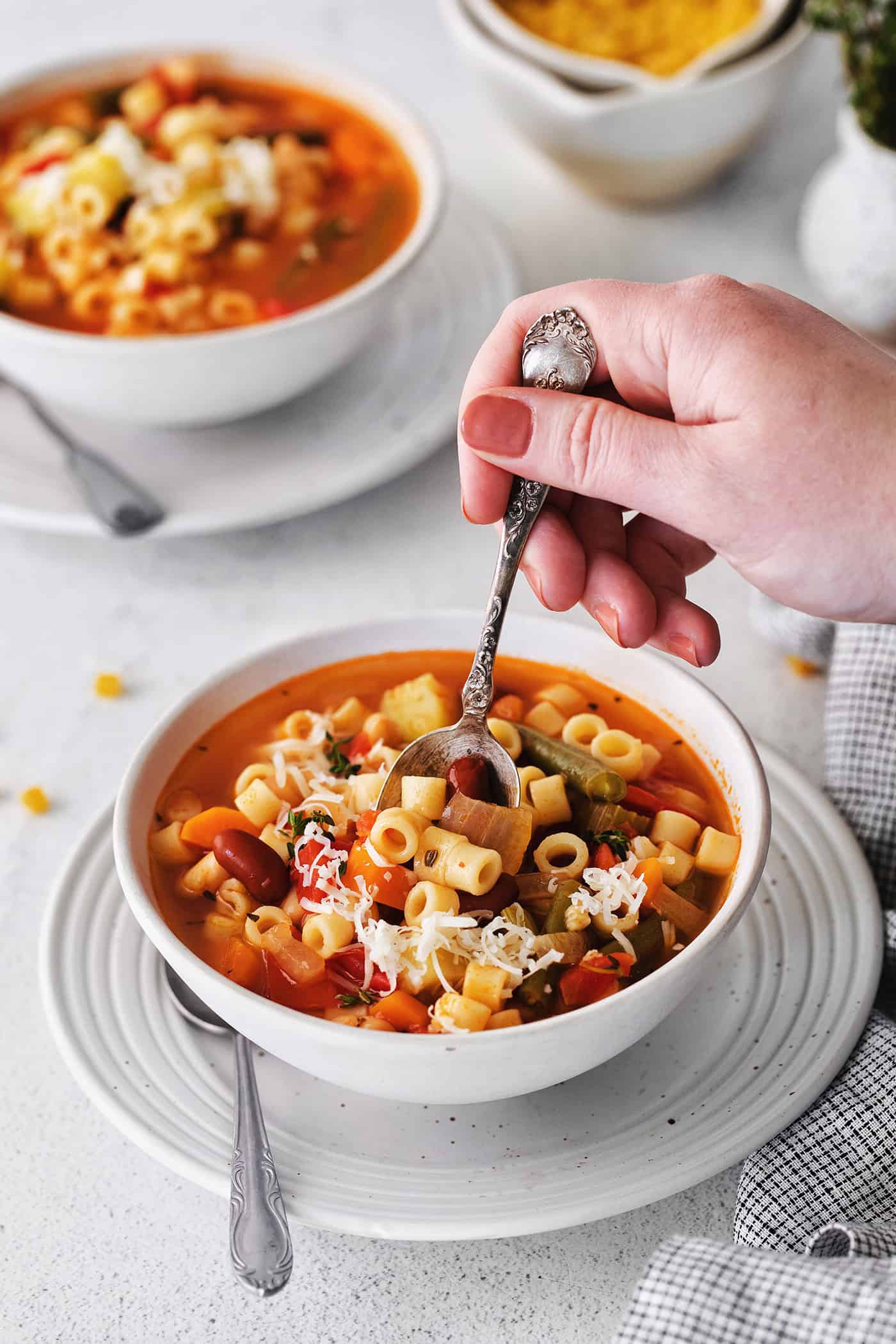 A hand with a spoon in a bowl of minestrone soup