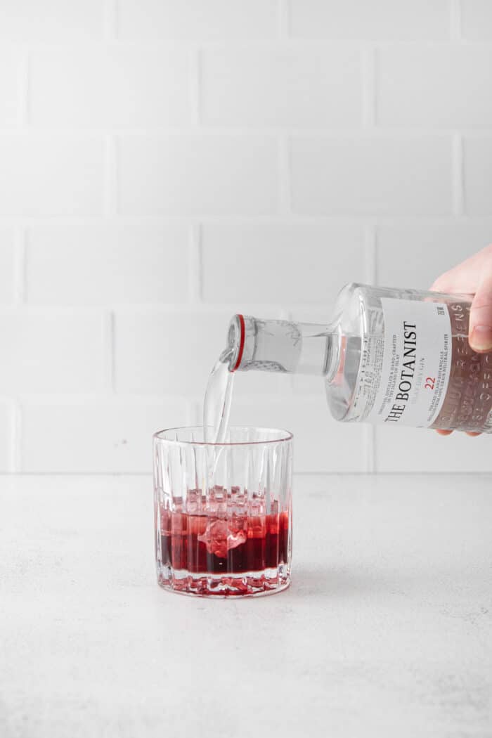 A hand pouring gin into a glass