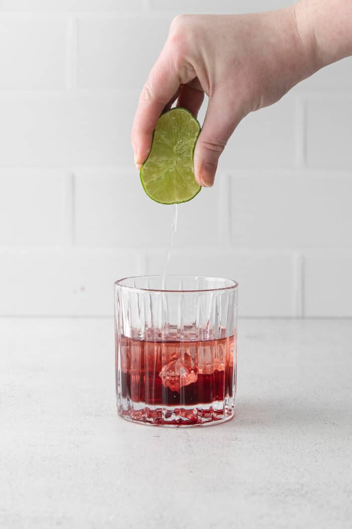 A hand squeezing lime into a glass with gin and pomegranate juice