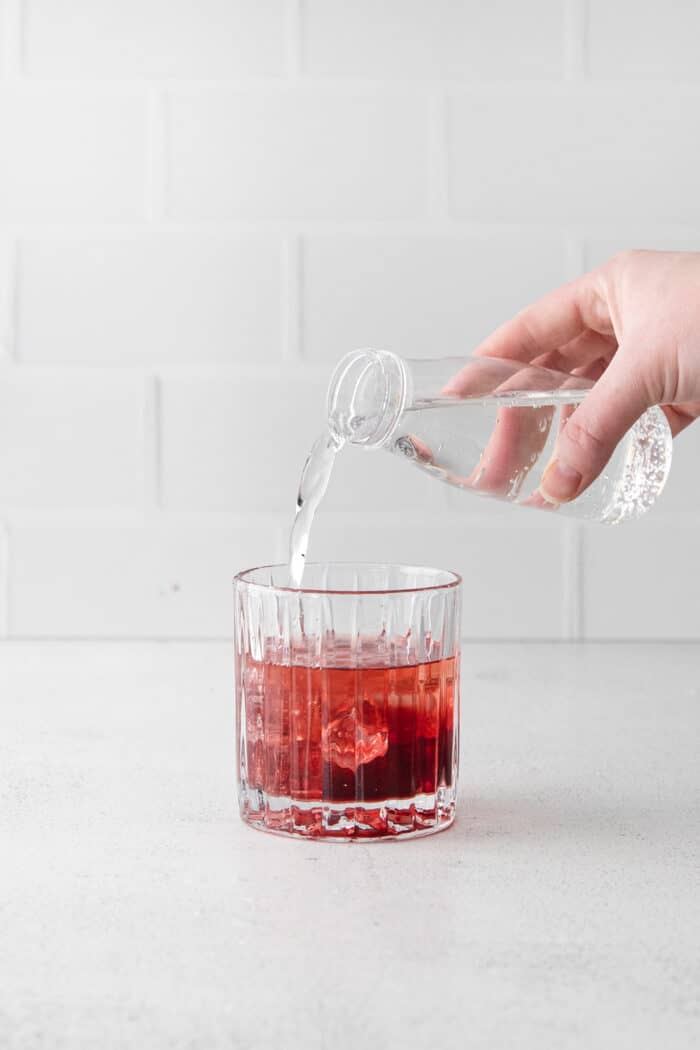A hand pouring tonic water into a glass with pomegranate juice