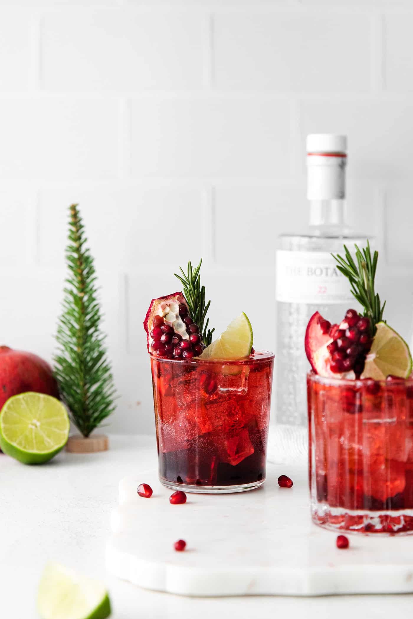 Two pomegranate gin and tonics in front of a bottle of gin