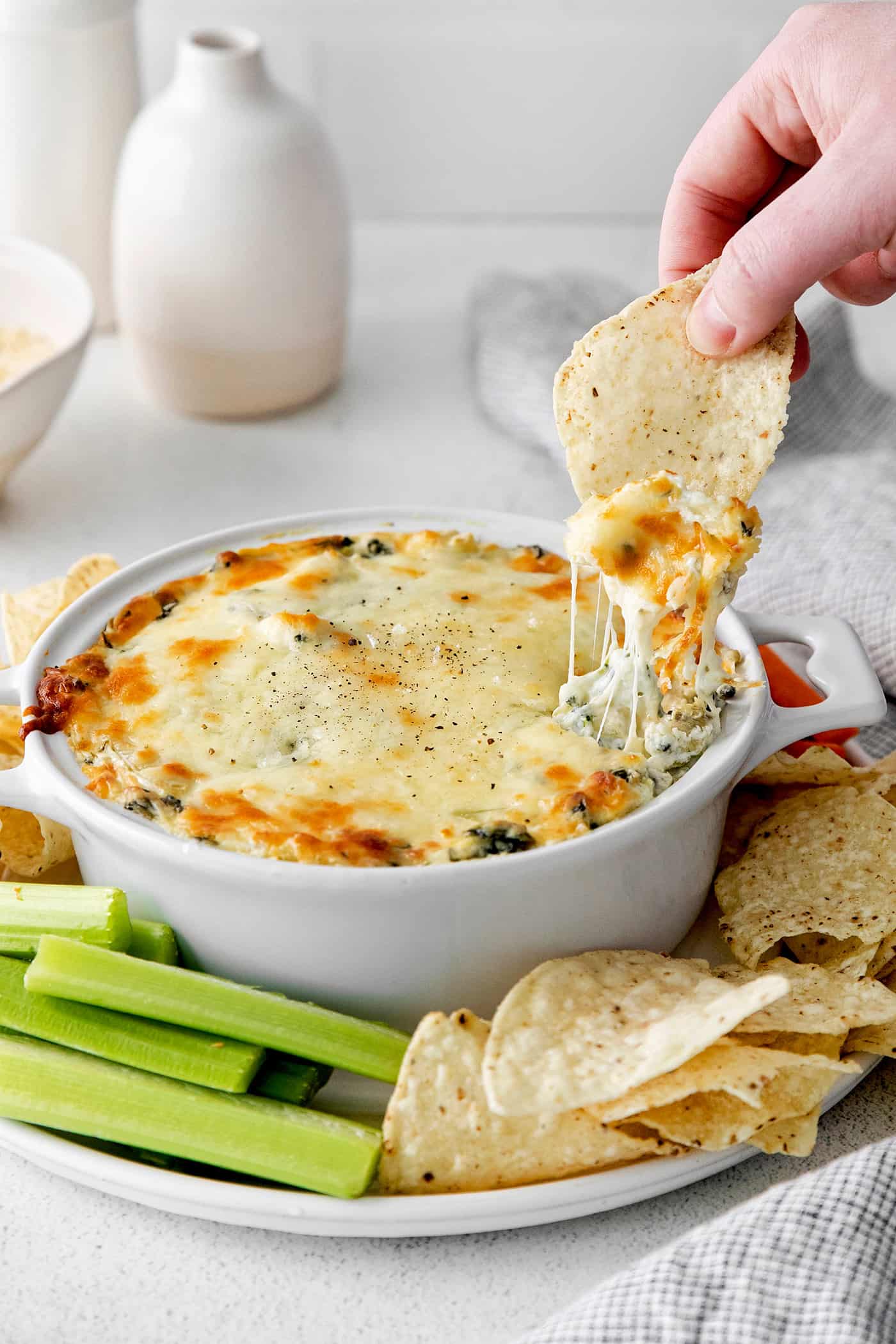 A hand dipping a chip into  a dish of spinach artichoke dip