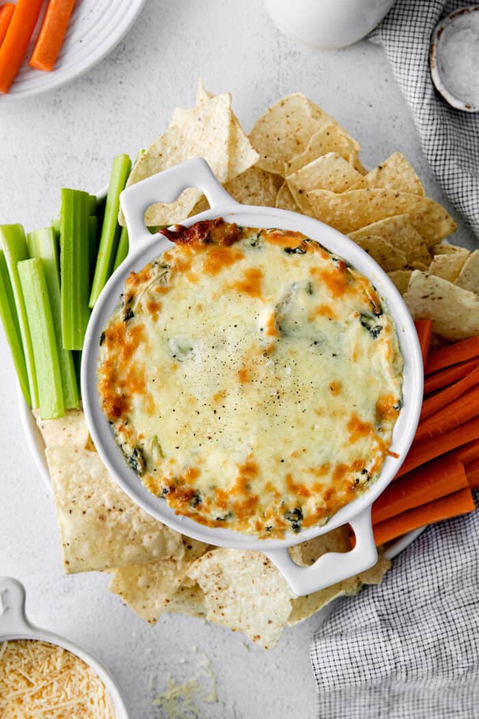 Overhead view of spinach artichoke dip on a plate with celery and peppers