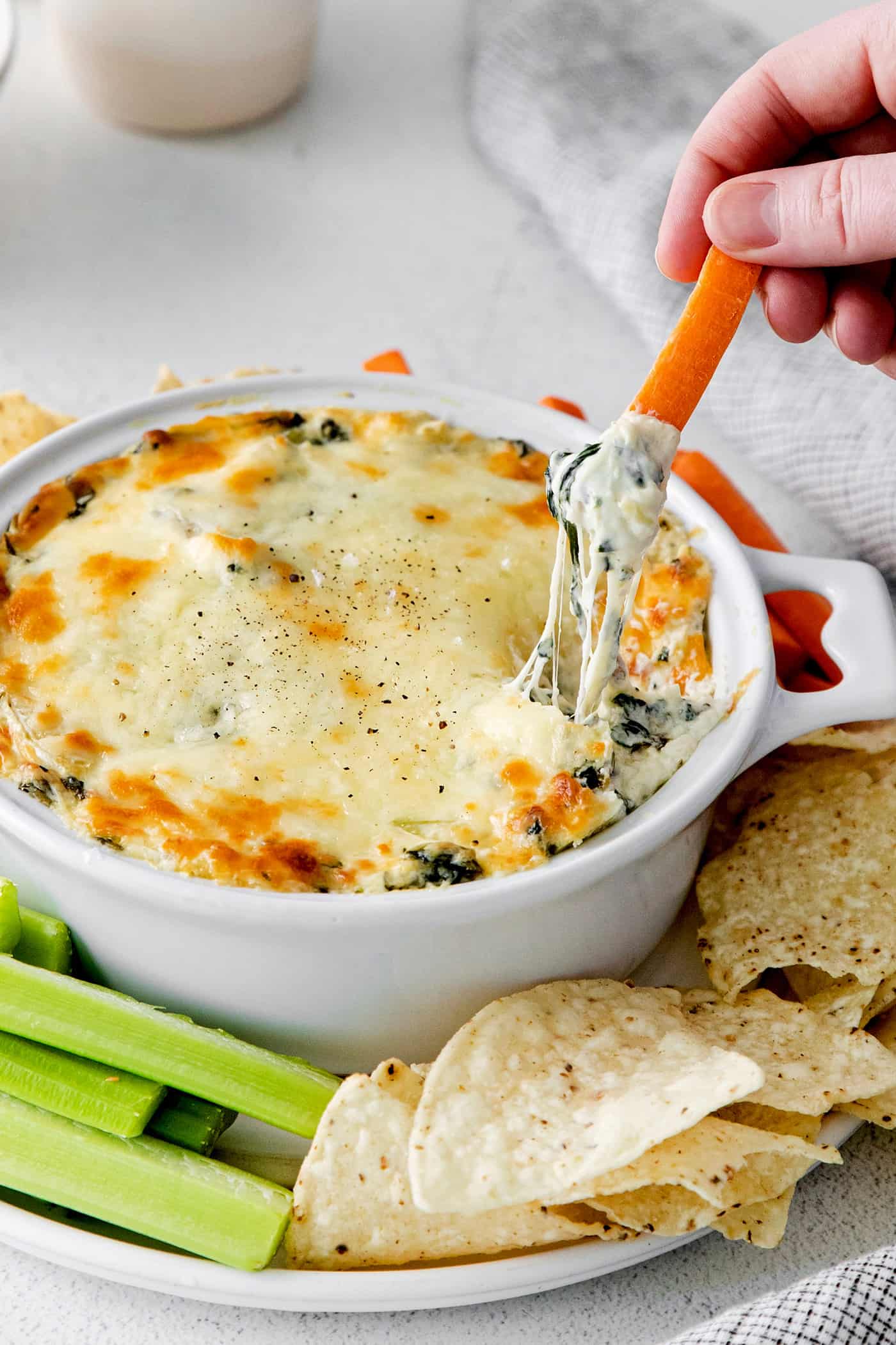 Overhead view of a hand dipping a carrot into spinach artichoke dip