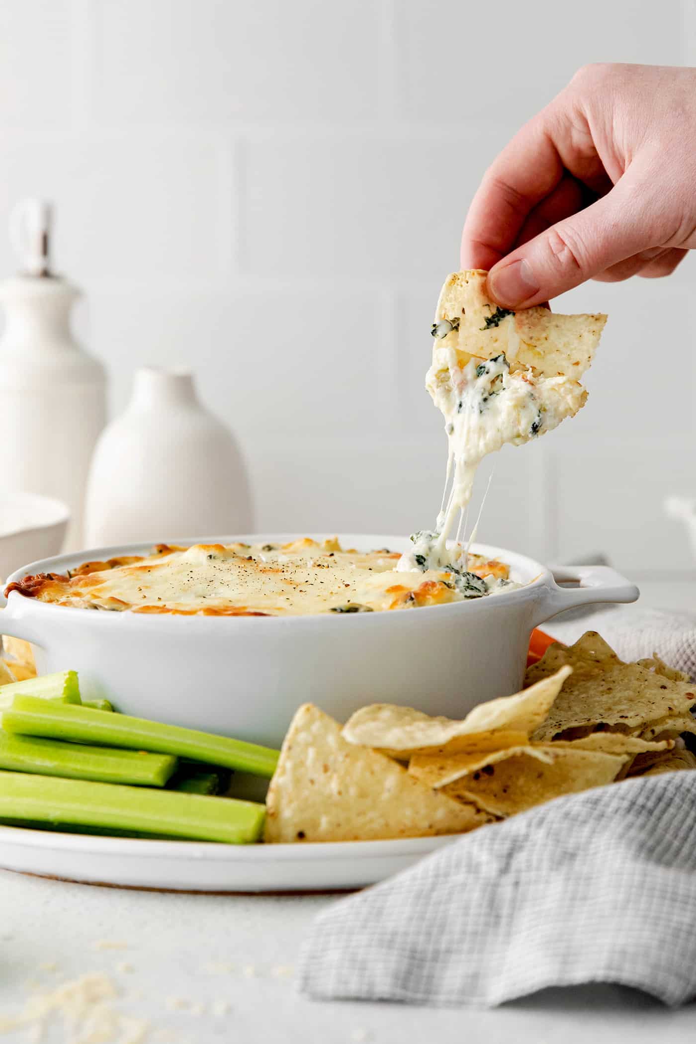 A hand dipping a chip into spinach artichoke dip