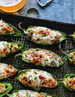 baked stuffed jalapenos with sausage and cheese on a pan, plus a glass of beer