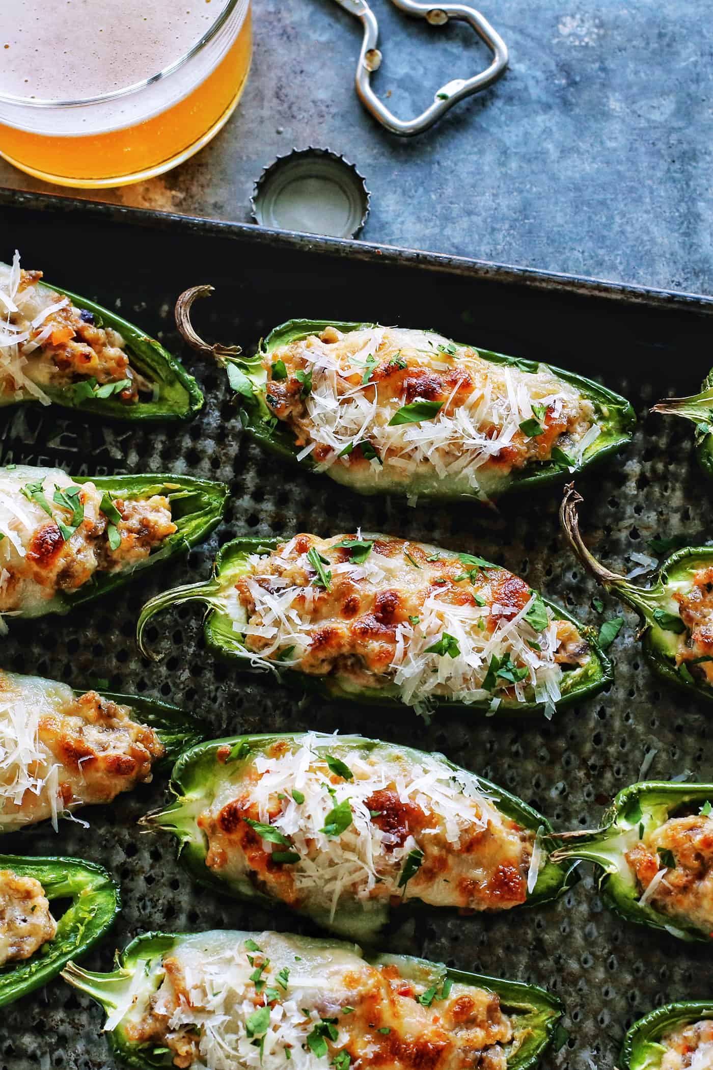 baked stuffed jalapenos with sausage and cheese on a pan, plus a glass of beer