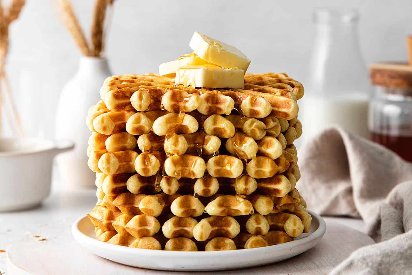 A stack of buttermilk waffles topped with butter on a white plate