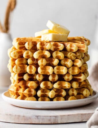 A stack of buttermilk waffles topped with butter on a white plate