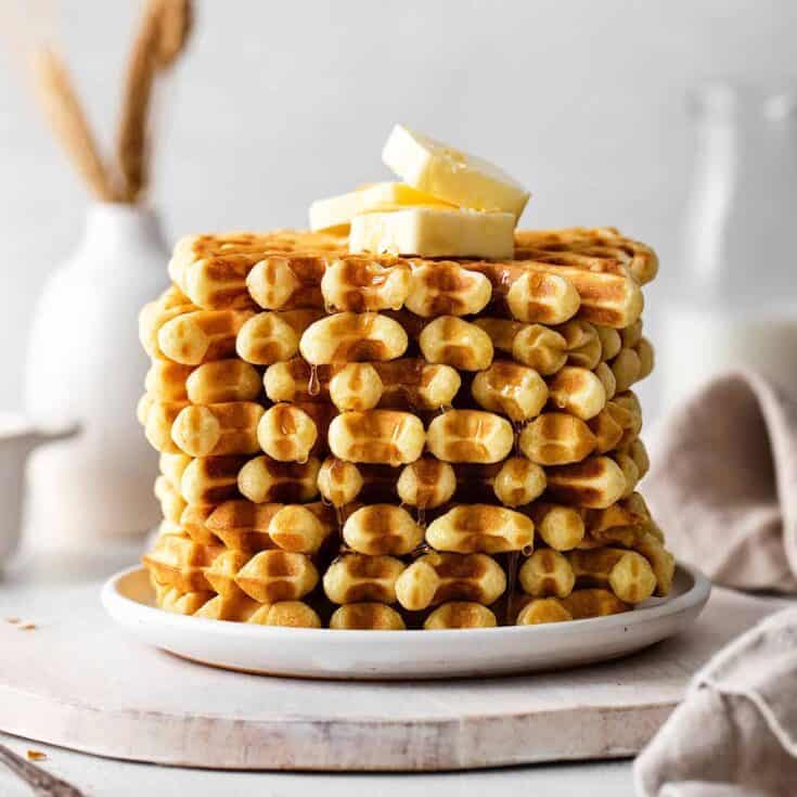 A stack of buttermilk waffles topped with butter on a white plate