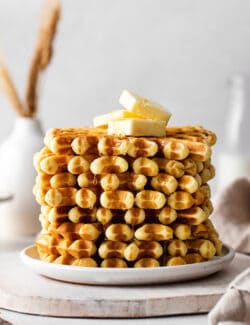 A stack of buttermilk waffles topped with butter on a white plate