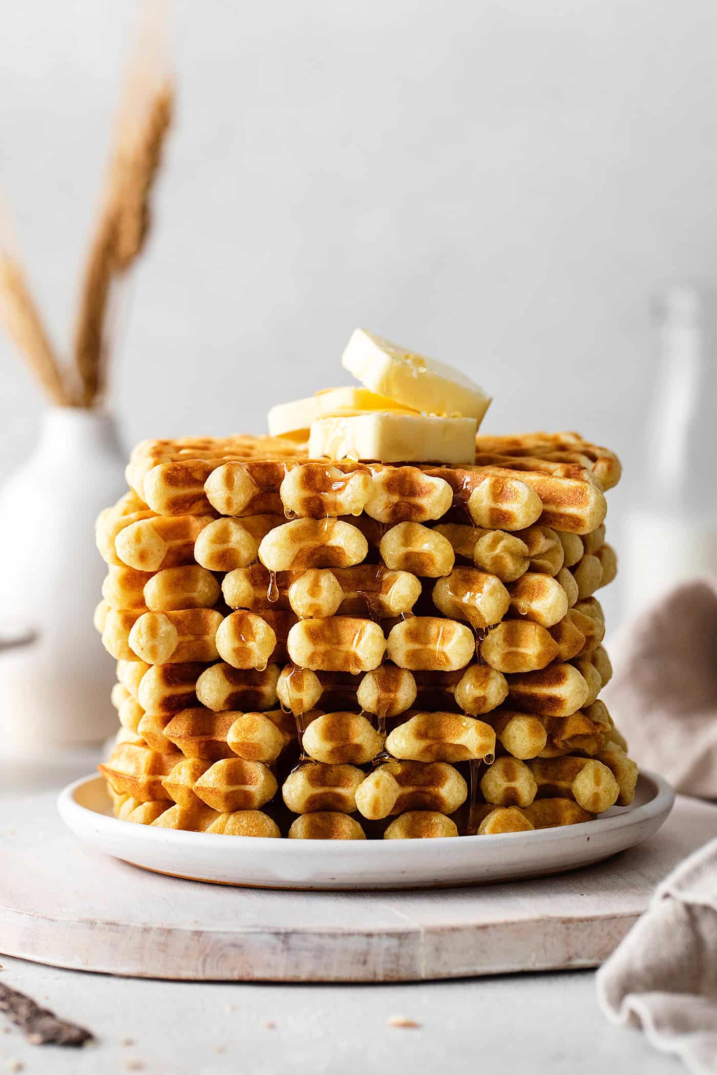 A stack of buttermilk waffles topped with butter on a white plate