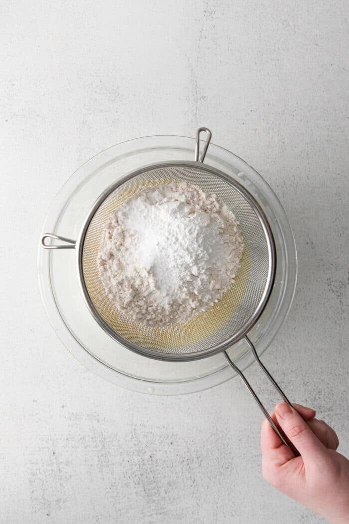 Flour being sifted into a bowl of buttermilk