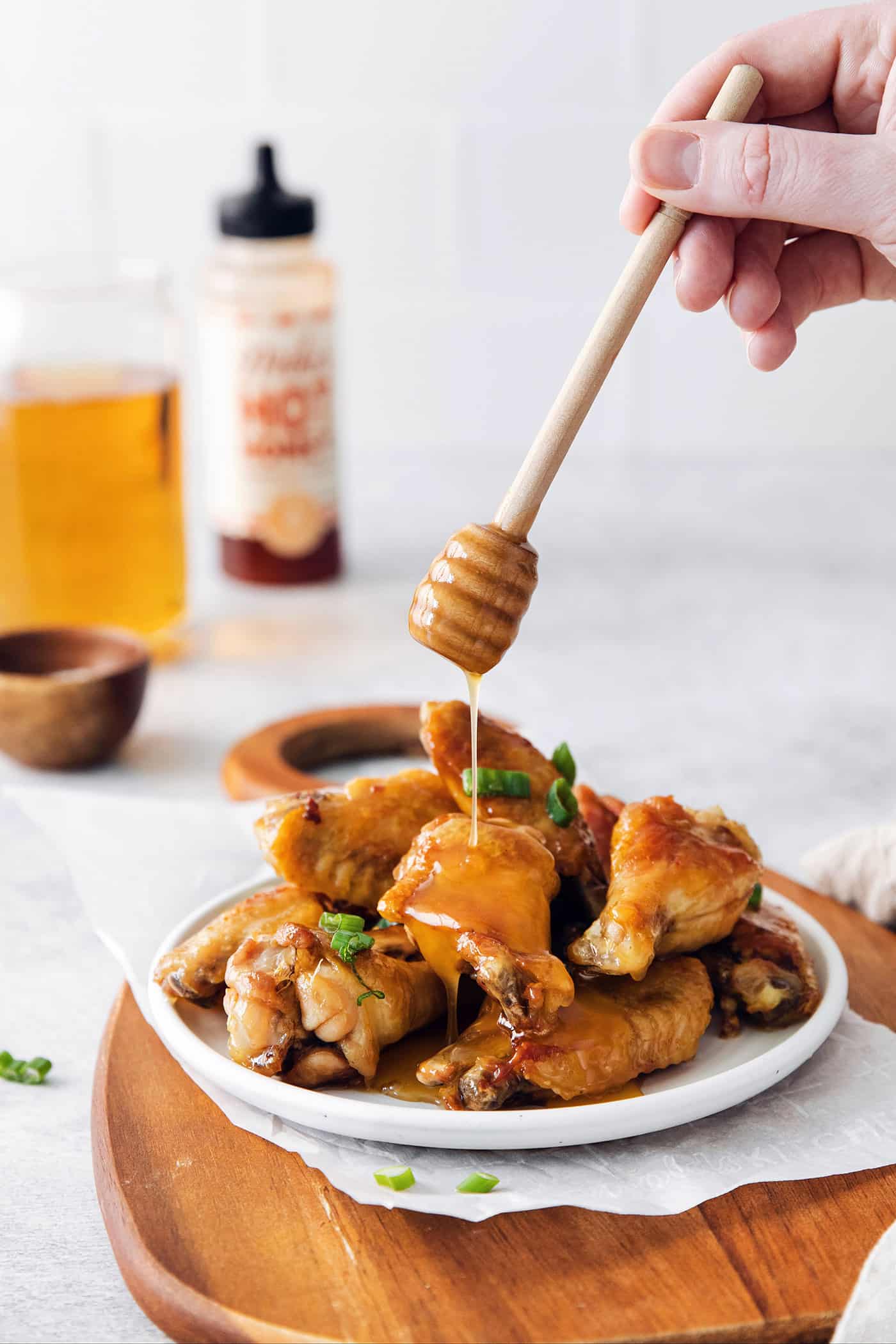 A hand drizzling honey over chicken wings