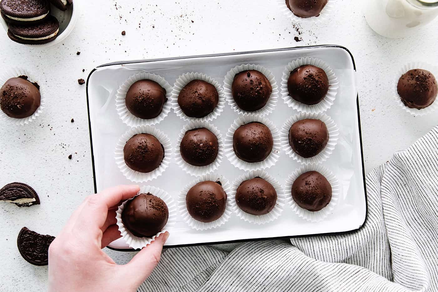 A hand grabbing Oreo truffles off from a baking sheet