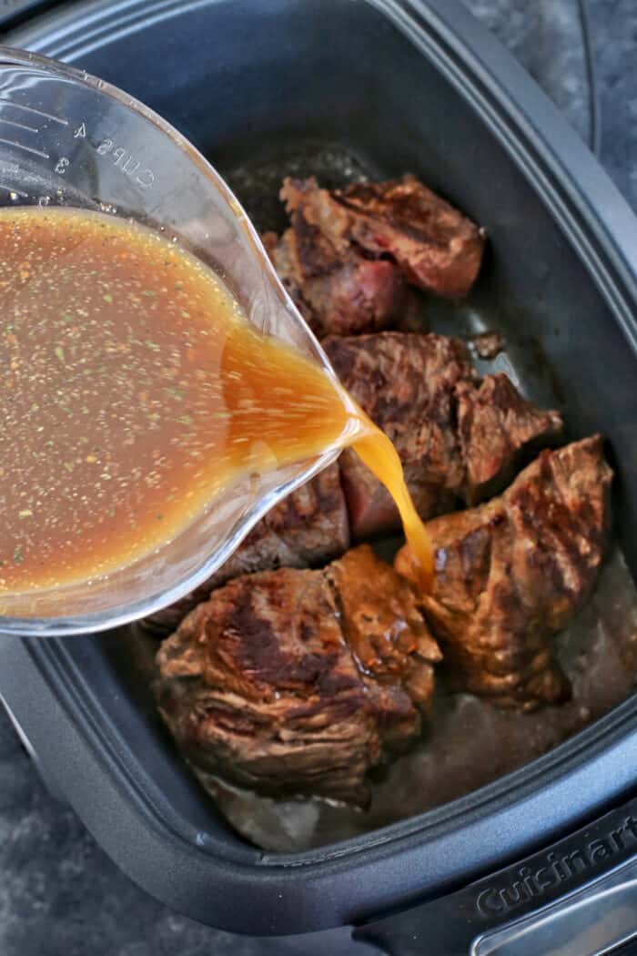 Italian seasoning and beef broth being poured over chuck roast