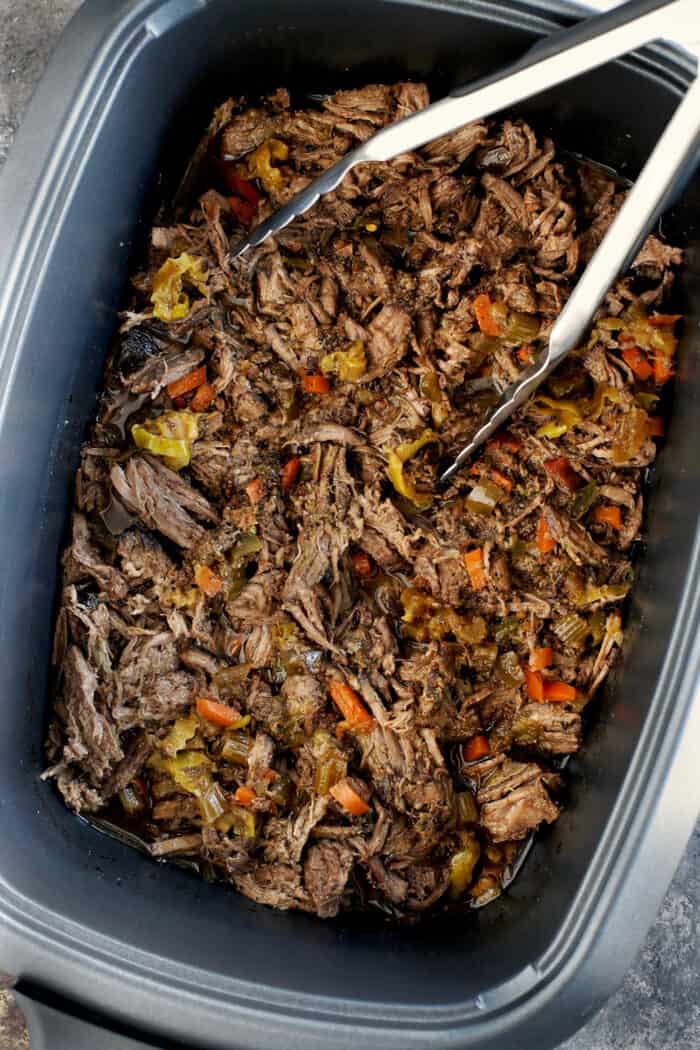 Tongs in a pan of shredded Italian beef