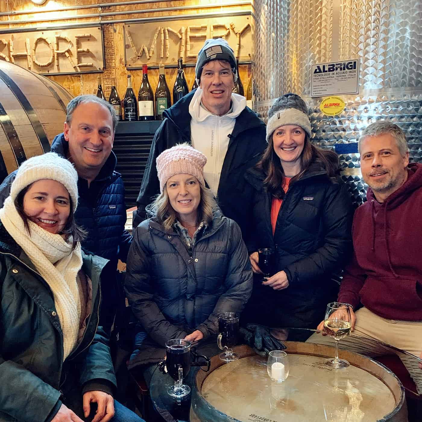 6 people in winter coats and hats enjoying a drink at a winery